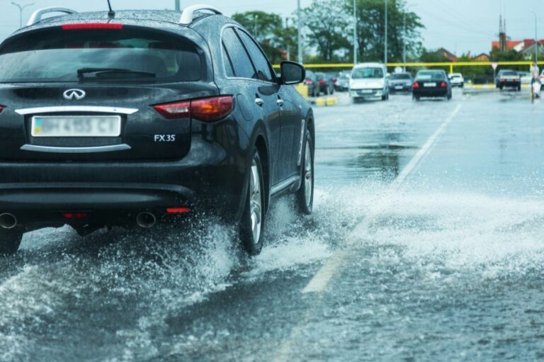 arafed car driving through a flooded street with water splashing over it