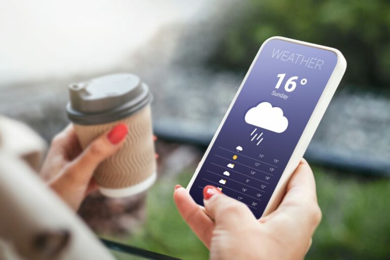 someone holding a smart phone with a weather app on the screen