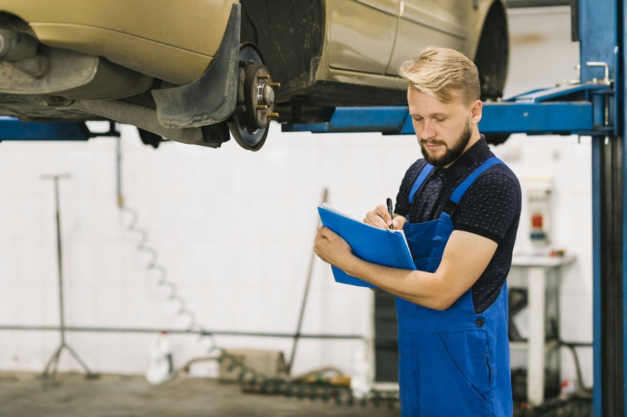 arafed man in blue overalls writing on a clipboard in front of a car