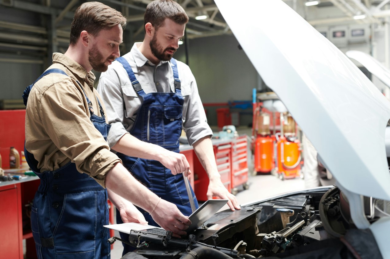 two men working on a car in a garage with a hood open